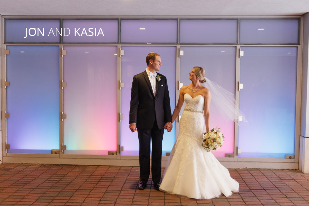 jon kasia | Jessica Miller Photography bride and groom holding hands in front of LED lights